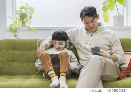親子の日常 イメージ スマートフォンを見る父親とタブレットを見る息子 親子の日常 イメージ スマートフォンを見る父親とタブレットを見る息子 109990334