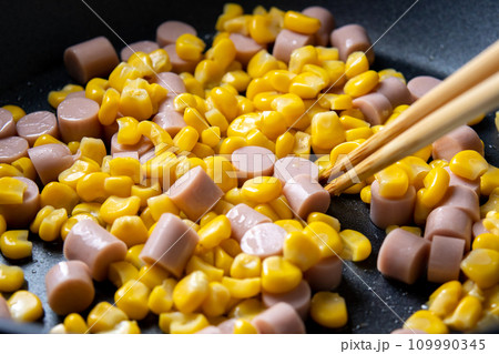 魚肉ソーセージと粒コーンを炒める調理シーン。 109990345
