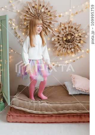 A little red-haired girl jumps on mattresses in a nursery decorated for the Christmas holidays. A little red-haired girl jumps on mattresses in a nursery decorated for the Christmas holidays. 109995759