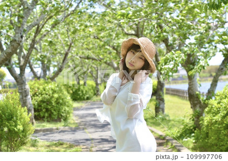 新緑の公園と麦わら帽子を被った若い女性 109997706