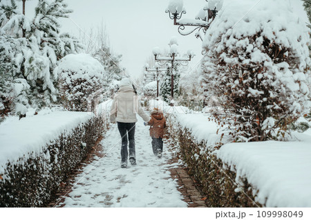 Happy cheerful mom with a child boy and son running backs in snow in winter in park 109998049