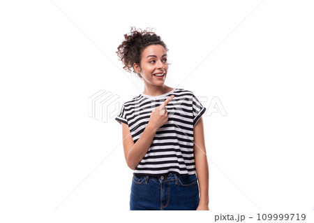 young well-groomed curly woman in a summer t-shirt points her finger on a white background 109999719