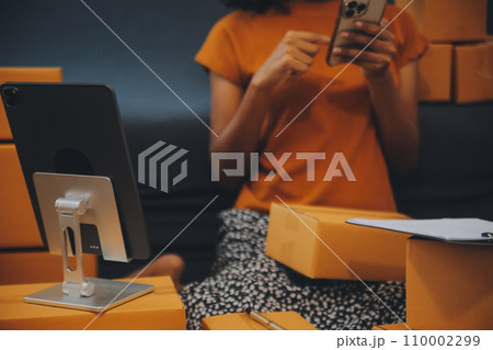 Startup SME small business entrepreneur of freelance Asian woman using a laptop with box Cheerful success happy Asian woman her hand lifts up online marketing packaging and delivery SME idea concept 110002299