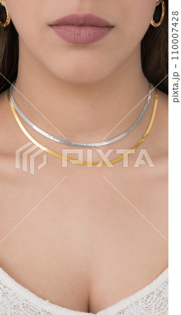 Young woman wearing golden earrings and a golden and a silver snake chain necklace. Young woman wearing golden earrings and a golden and a silver snake chain necklace. 110007428