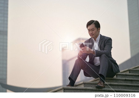 asian corporate executive sitting on steps looking at mobile phone 110009316