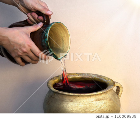 A hand holds a clay jar and pours water 110009839
