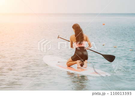 Sea woman sup. Silhouette of happy young woman in pink bikini, surfing on SUP board, confident paddling through water surface. Idyllic sunset. Active lifestyle at sea or river. Sea woman sup. Silhouette of happy young woman in pink bikini, surfing on SUP board, confident paddling through water surface. Idyllic sunset. Active lifestyle at sea or river. 110013393