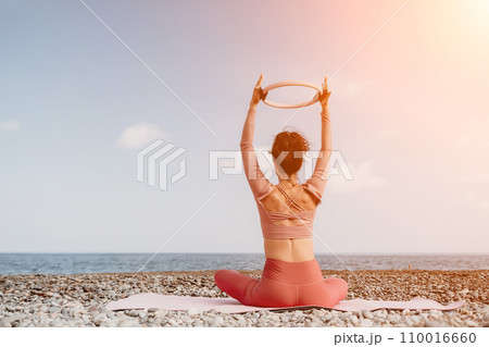 Woman sea pilates. Sporty happy middle aged woman practicing fitness on beach near sea, smiling active female training with ring on yoga mat outside, enjoying healthy lifestyle, harmony and meditation 110016660