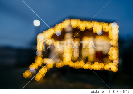 Abstract defocused bright Christmas lights on wooden house, creating decorative illumination in evening scene 110016677