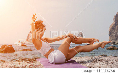 Fitness woman sea. A happy middle aged woman in white sportswear exercises morning outdoors on a beach with volcanic rocks by the sea. Female fitness pilates yoga routine concept. Healthy lifestyle. Fitness woman sea. A happy middle aged woman in white sportswear exercises morning outdoors on a beach with volcanic rocks by the sea. Female fitness pilates yoga routine concept. Healthy lifestyle. 110016736