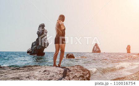 Woman summer travel sea. Happy tourist in hat enjoy taking picture outdoors for memories. Woman traveler posing on the beach at sea surrounded by volcanic mountains, sharing travel adventure journey 110016754