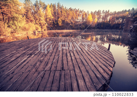 Magical sunrise over the lake. Pine trees on the lakeshore. Serene lake in the early morning. Wooden round pier on the lake. Nature landscape. 110022833