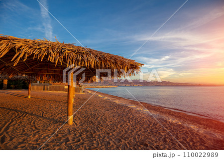 Tropical beach scenery with sun parasols. Straw sun umbrellas on the beach at sunset. Eilat, Israel Tropical beach scenery with sun parasols. Straw sun umbrellas on the beach at sunset. Eilat, Israel 110022989