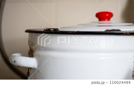 One large white pot with a lid and a red handle sits on a tile in a restaurant or home kitchen One large white pot with a lid and a red handle sits on a tile in a restaurant or home kitchen 110024494