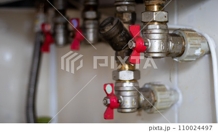 Hidden water taps for connecting a gas boiler on a tiled wall. Plumbing connections for a domestic double-circuit gas boiler. Pipes of the heating system. Installing a gas boiler with red taps 110024497