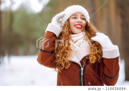 Beautiful woman standing among snowy trees and enjoying first snow. Holidays, rest, travel concept. 110026884