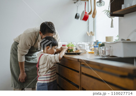 キッチンでハンバーガーを作る7歳の男の子と見守る父親 110027714