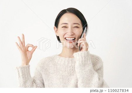 スマホで通話をしながらOKサインをする中年女性　白背景 110027834