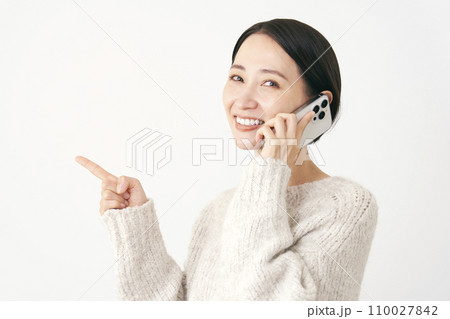 スマホで通話をしながら左側を指差す中年女性 白背景 スマホで通話をしながら左側を指差す中年女性 白背景 110027842