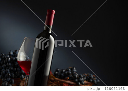 Bottle and glass of red wine with blue grapes on a black background. Bottle and glass of red wine with blue grapes on a black background. 110031168