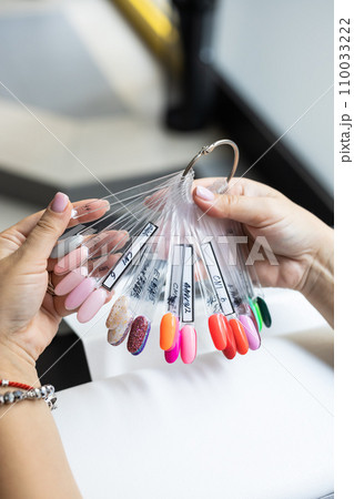Collection of nails color polish samples. A palette of nail designs of different colors with gel polish. Transparent tips with nail polish samples. Demonstration fan-shaped palette of color shades. 110033222