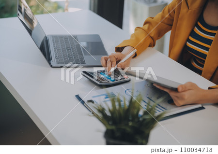 Charming Young asian businesswoman sitting on laptop computer in the office, making report calculating balance Internal Revenue Service checking document. 110034718