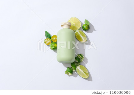 An unlabeled cosmetic bottle is placed in the center of a white background, surrounded by fresh lemons and kumquats. Skin care with natural cosmetics. An unlabeled cosmetic bottle is placed in the center of a white background, surrounded by fresh lemons and kumquats. Skin care with natural cosmetics. 110036006