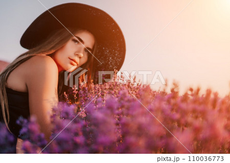 Woman lavender field. Happy carefree woman in black dress and hat with large brim smelling a blooming lavender on sunset. Perfect for inspirational and warm concepts in travel and wanderlust. Close up Woman lavender field. Happy carefree woman in black dress and hat with large brim smelling a blooming lavender on sunset. Perfect for inspirational and warm concepts in travel and wanderlust. Close up 110036773
