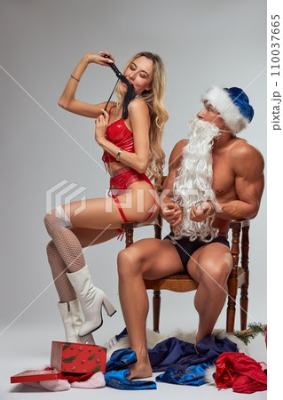 Sexy woman biting a whip while sitting on a chair with Santa Claus 110037665