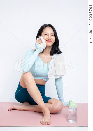 There is a woman who wipes her forehead with a towel on a yoga mat 110038701