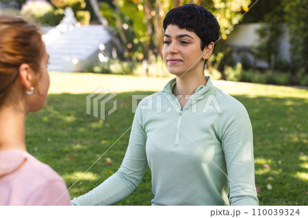 Happy biracial lesbian couple practicing yoga meditation sitting stretching in sunny garden Happy biracial lesbian couple practicing yoga meditation sitting stretching in sunny garden 110039324