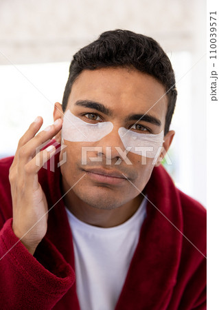Happy biracial man applying uder-eye patches in bathroom at home 110039571
