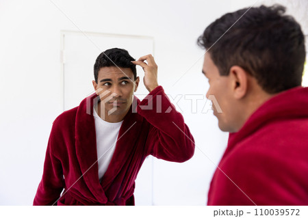 Happy biracial man touching his hair looking in mirror in bathroom at home 110039572