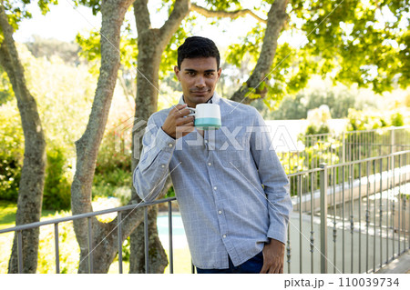 Portrait of happy biracial man holding mug on balcony at home Portrait of happy biracial man holding mug on balcony at home 110039734