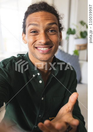 Happy biracial man with long curly hair having video call and smiling in sunny living room at home Happy biracial man with long curly hair having video call and smiling in sunny living room at home 110039997