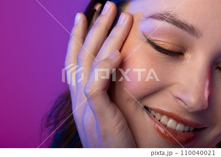 Caucasian woman wearing eyeliner and lip gloss on purple background Caucasian woman wearing eyeliner and lip gloss on purple background 110040021