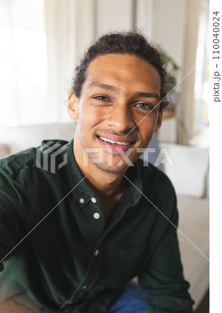 Happy biracial man with long curly hair having video call and smiling in sunny living room at home Happy biracial man with long curly hair having video call and smiling in sunny living room at home 110040024
