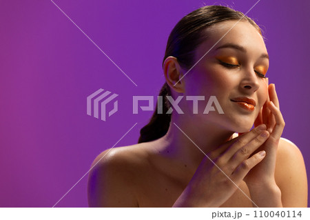 Caucasian woman wearing orange eye shadow and lip gloss on purple background, copy space Caucasian woman wearing orange eye shadow and lip gloss on purple background, copy space 110040114