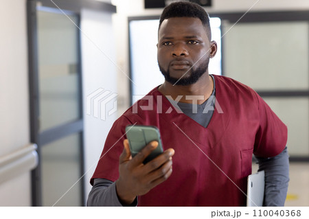 African american male doctor using smartphone in hospital corridor 110040368
