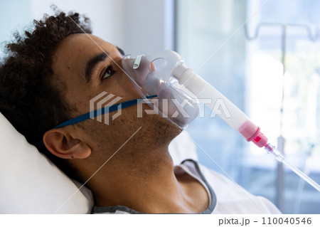 Biracial male patient with oxygen mask lying in bed in sunny hospital room 110040546
