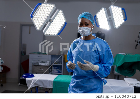 Portrait of african american female doctor with face mask and gloves in hospital operating room 110040712