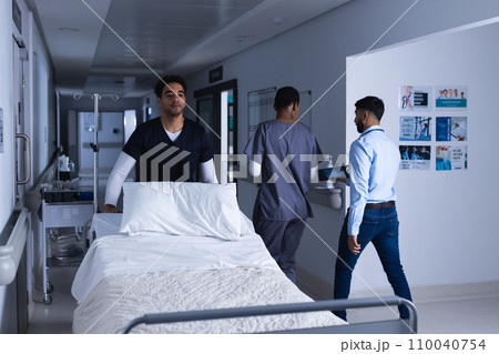 Biracial male doctor walking with bed in hospital corridor Biracial male doctor walking with bed in hospital corridor 110040754