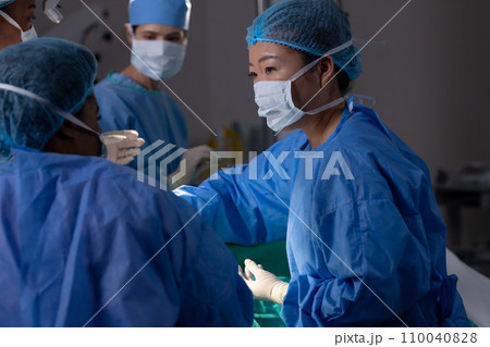 Diverse female doctors with face masks doing surgery in hospital operating room Diverse female doctors with face masks doing surgery in hospital operating room 110040828