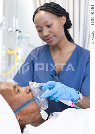 African american female doctor applying oxygen mask to senior female patient in hospital room 110040961