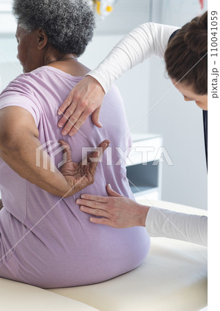 Diverse female doctor testing back of senior female patient in hospital room 110041059