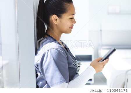 Biracial female doctor wearing scrubs using smartphon in hospital Biracial female doctor wearing scrubs using smartphon in hospital 110041171