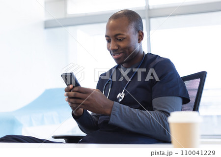 Happy african american male doctor using smartphone at desk in hospital Happy african american male doctor using smartphone at desk in hospital 110041229