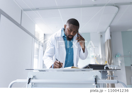African american male doctor talking on smartphone and taking notes in hospital room African american male doctor talking on smartphone and taking notes in hospital room 110041236