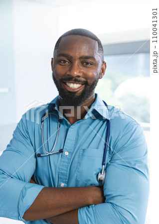 Portrait of happy african american male doctor wearing blue shirt and stethoscope in hospital room Portrait of happy african american male doctor wearing blue shirt and stethoscope in hospital room 110041301