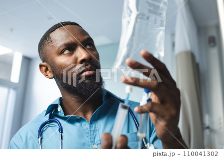African american male doctor wearing blue shirt applying drip in hospital room African american male doctor wearing blue shirt applying drip in hospital room 110041302